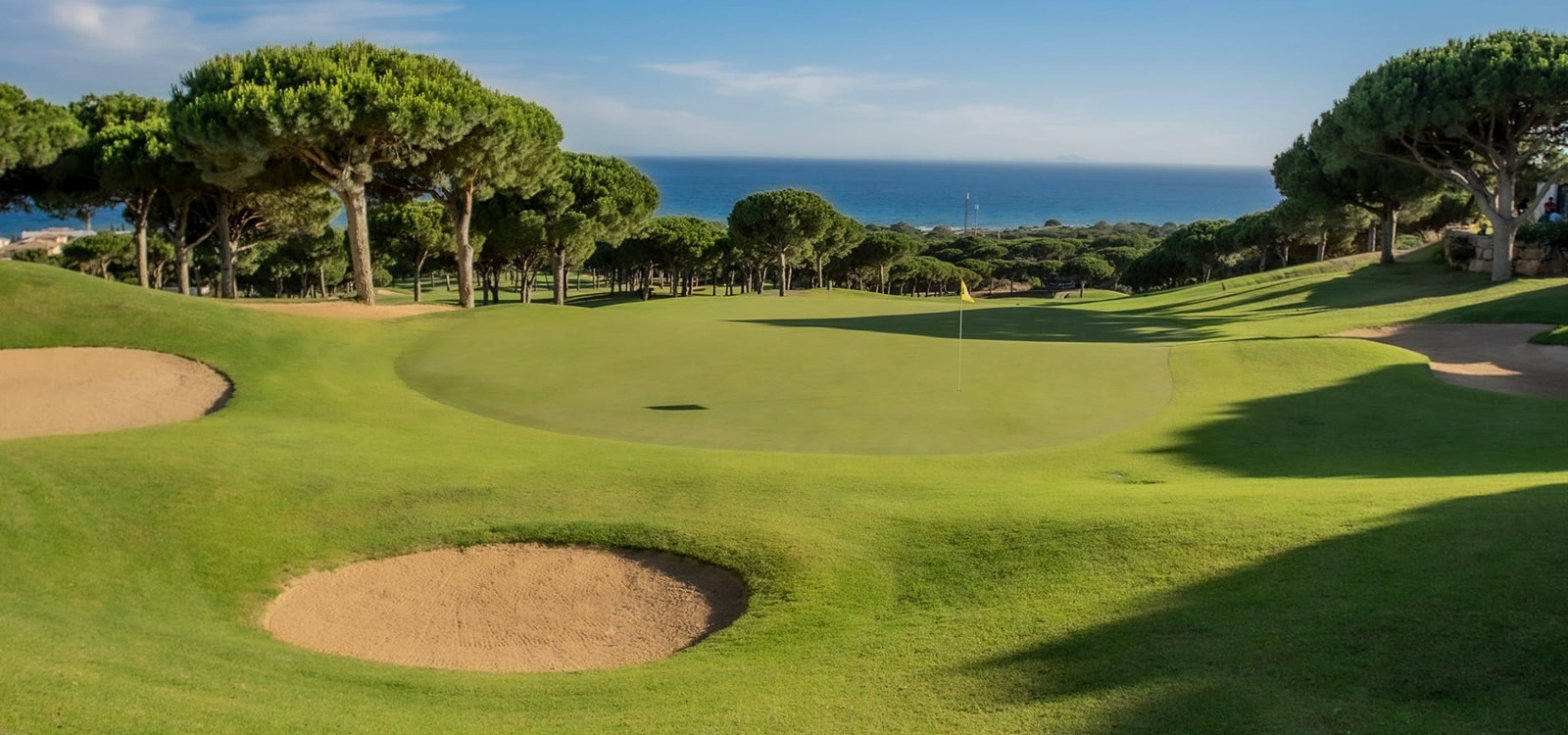 Elevated green at Cabopino Golf Marbella framed by pine trees with the Mediterranean beyond